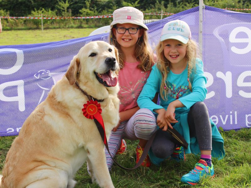 Two children sat next to a Golden Retriever in a field with the dog rosette
