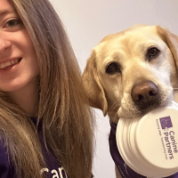 Selfie of dog and handler with dog holding purple Canine Partners bowl in its mouth