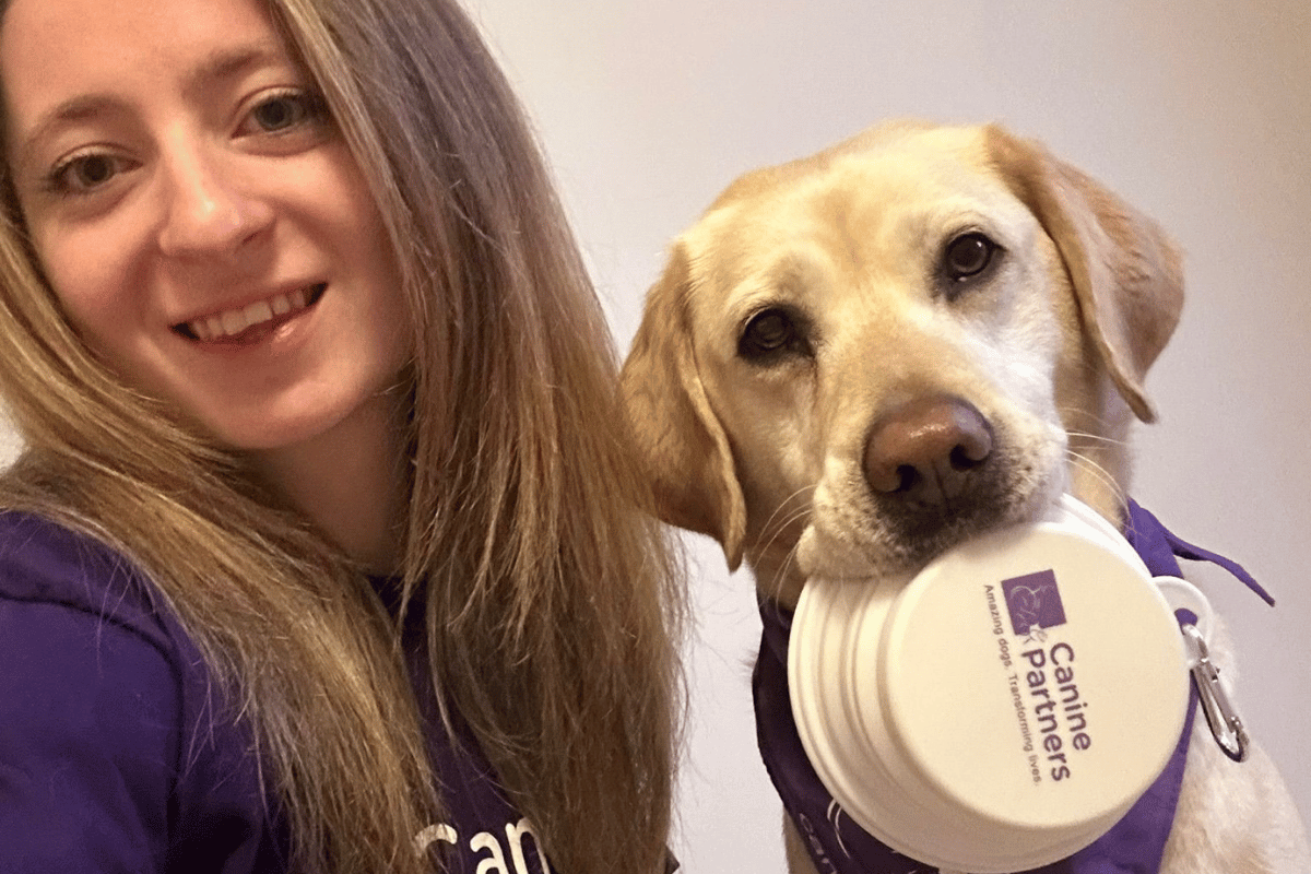 Selfie of dog and handler with dog holding purple Canine Partners bowl in its mouth