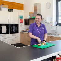 Housekeeping staff member cutting up food in the accommodation block kitchen at the National Training Centre
