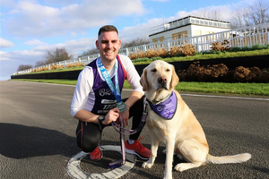 Photo of man crouching next to dog with bandanna on on a race track
