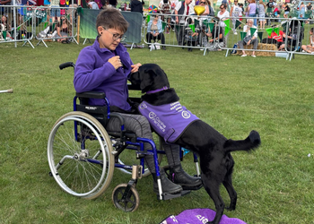 Photo of lady sat in a wheelchair at an event with black dog ambassador taking off her jacket