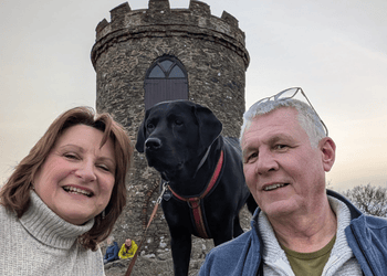 Selfie of two volunteers with the black Labrador and castle behind them