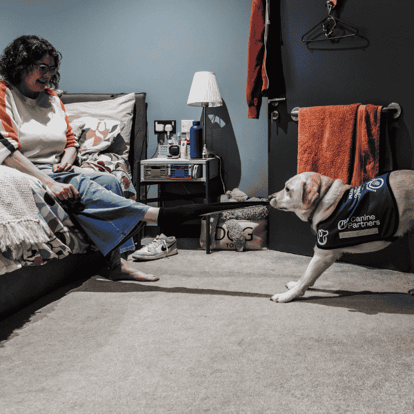 Photo of lady sat on bed with assistance dog tugging off her sock